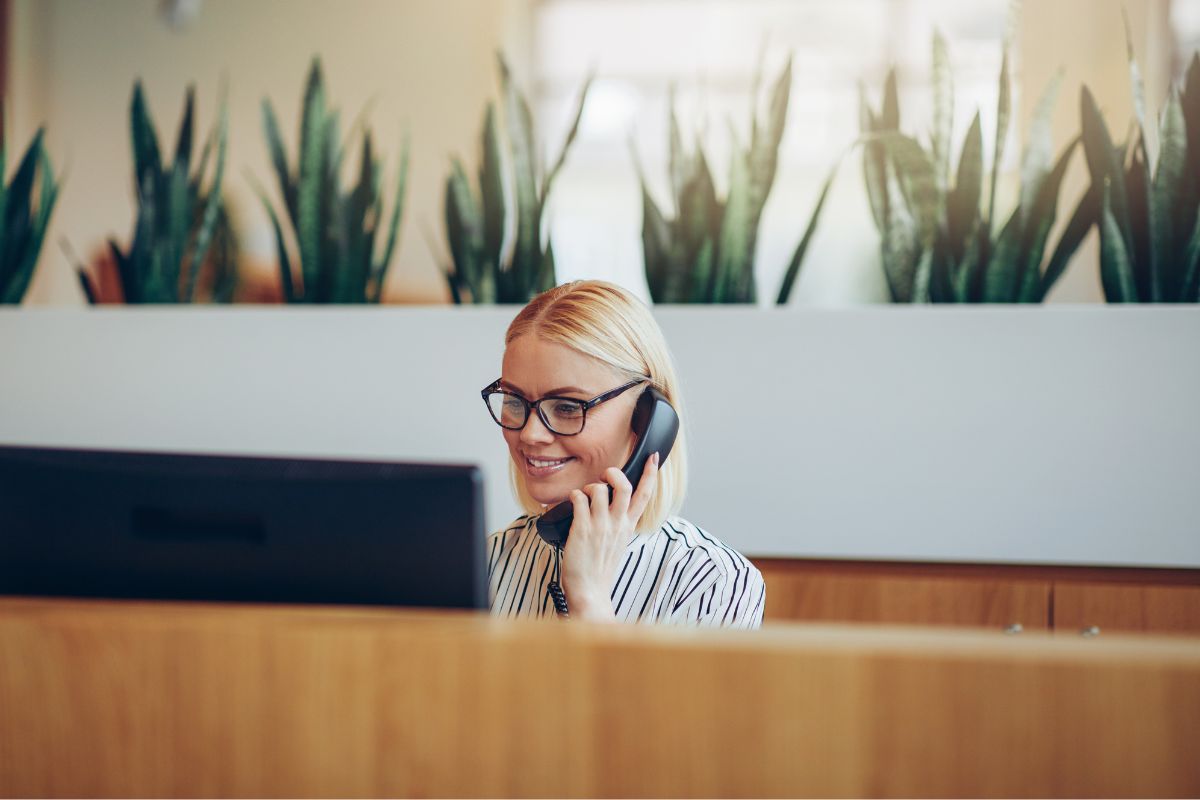 Eine blonde Frau an einem Computer am Telefon, welche mit Kunden in Kontakt steht und tellefoniert.